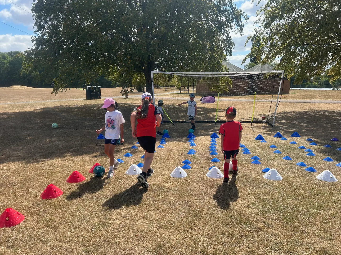 Children practising with footballs between coloured cones at a Football Frenzy holiday session
