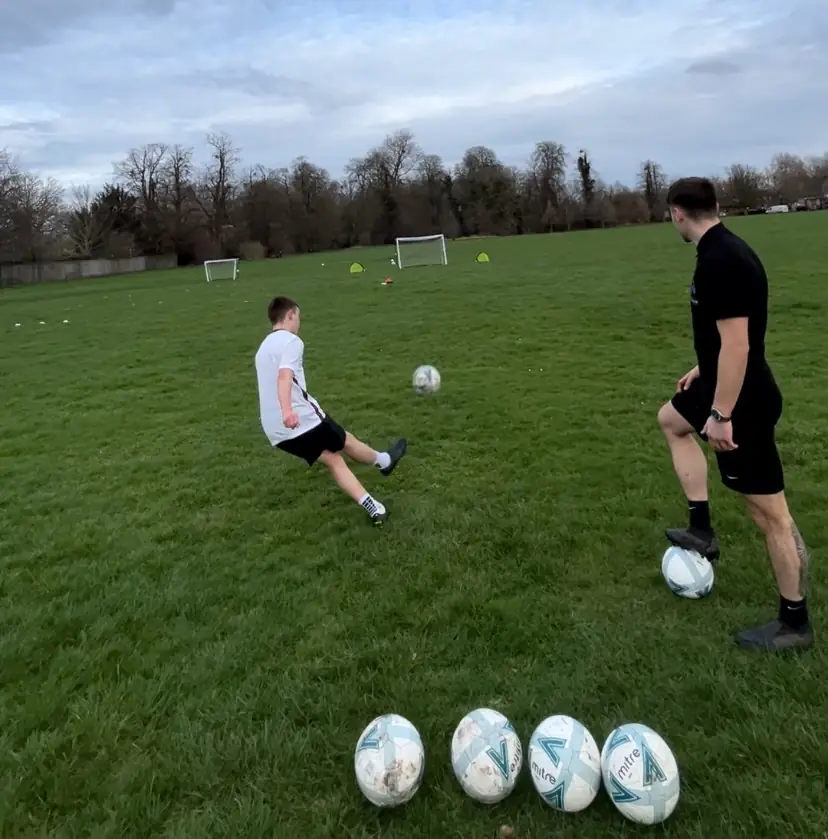 A player practising a kick with a Football Frenzy coach watching